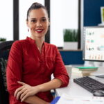 Portrait of business woman in corporate office sitting at desk smiling at camera. Company executive leadership working on financial statistics. worker doing charts on computer.